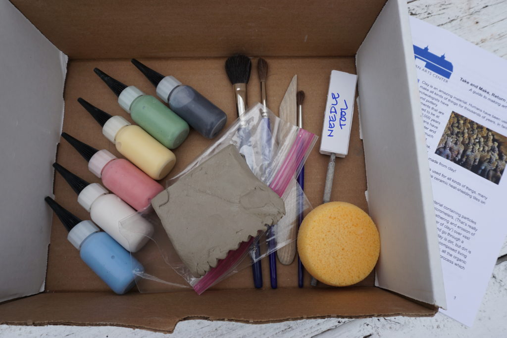 Shows the inside of a clay kit box with glaze bottles, brushes, tools, clay and instruction booklet on the side.